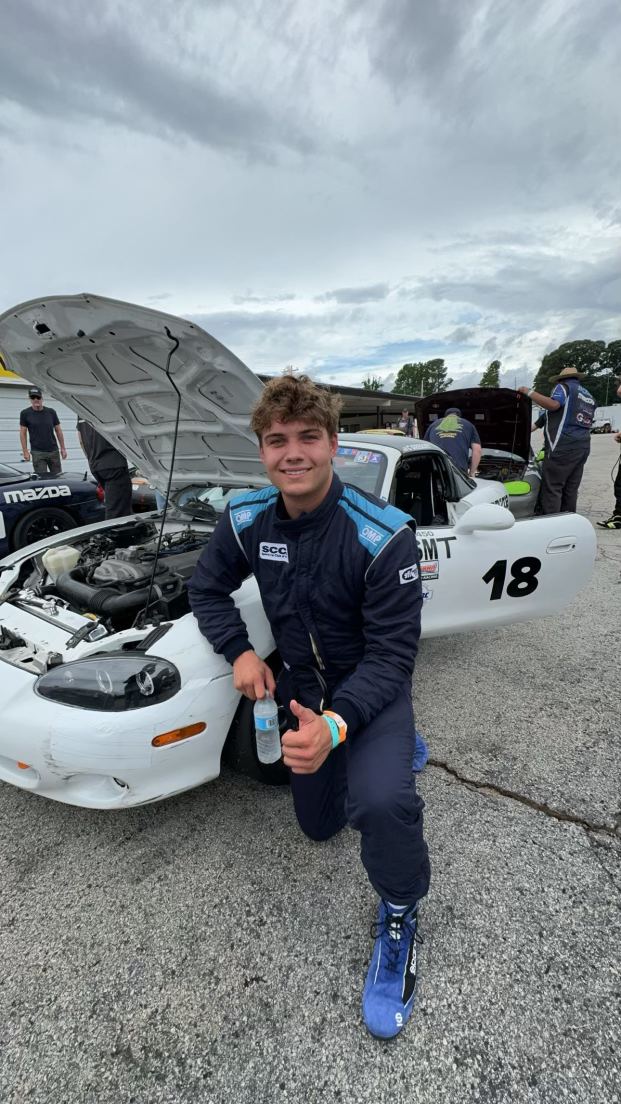 Carsten kneeling beside his home-built #18 Spec Miata in the paddock